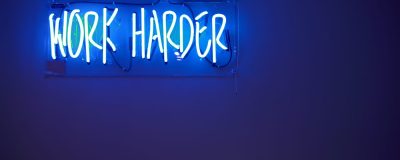 Work harder -valokyltti seinällä.