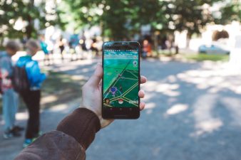 Kädessä pidetään pihalla puhelinta, jossa on auki Pokemon Go.